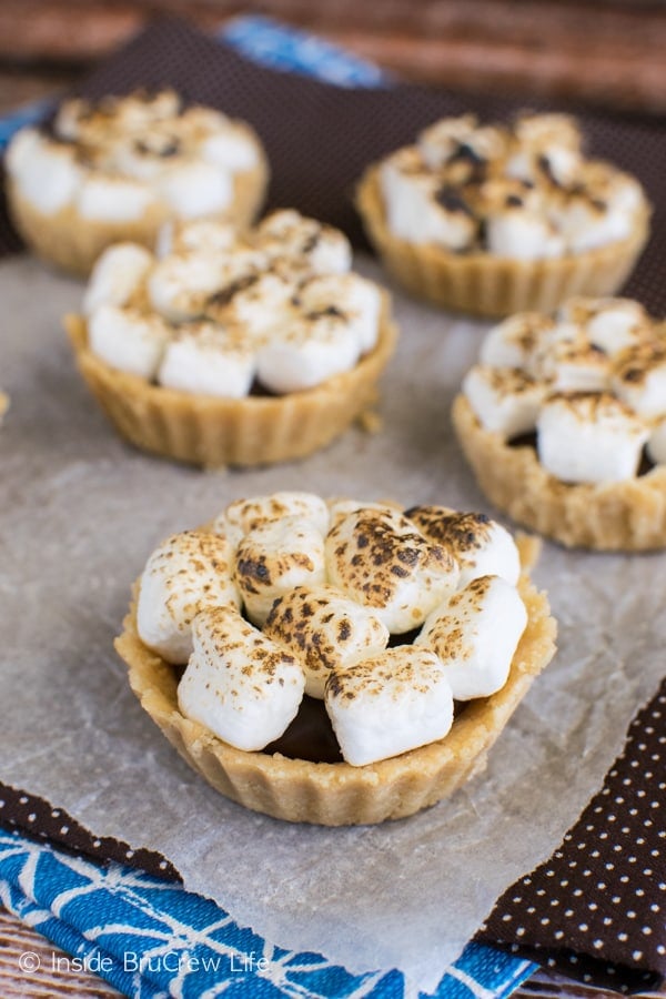 Five mini s'mores pies on parchment and a brown towel