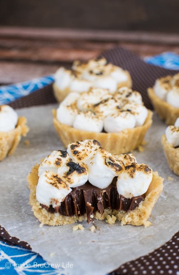 Mini s'mores pies on parchment paper with one cut in half with a fork showing the chocolate filling inside