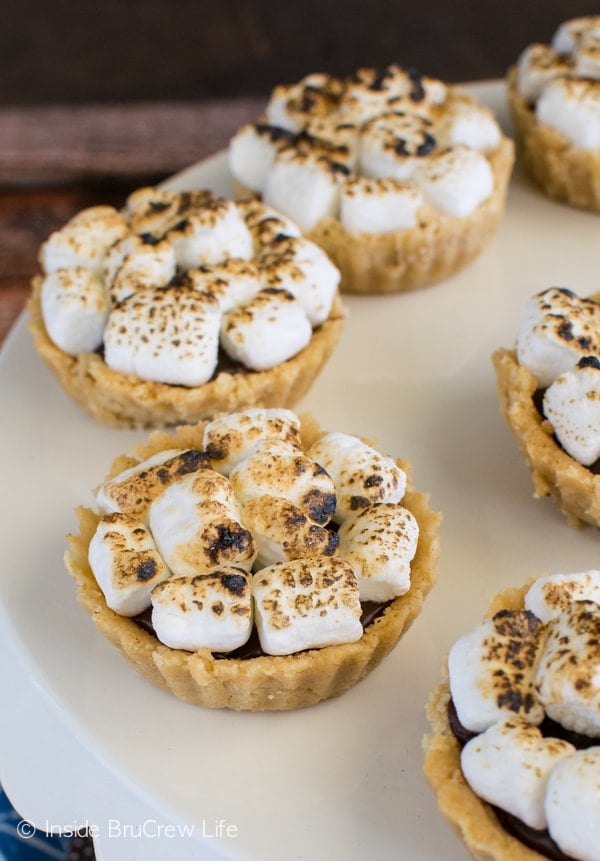 A white cake plate with mini s'mores pies with toasted marshmallows on them