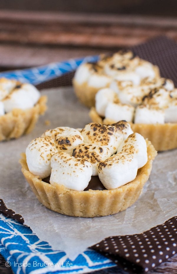 Parchment paper on a brown towel with four mini s'mores pies with toasted marshmallows on it