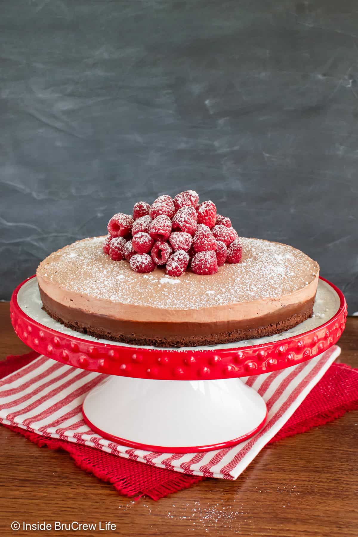 A red and white cake plate with a full Nutella mousse cake on it.
