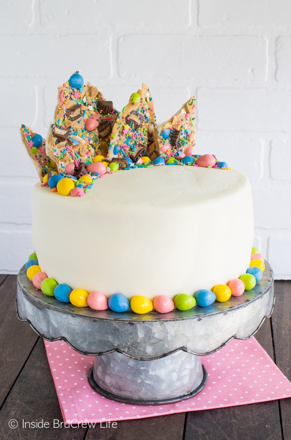 A full size cake with white frosting topped with colorful Easter candies on a metal cake plate.