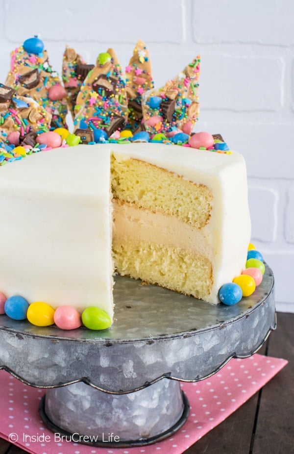 A white cake missing one slice with white frosting topped with colorful Easter candies on a metal cake plate.