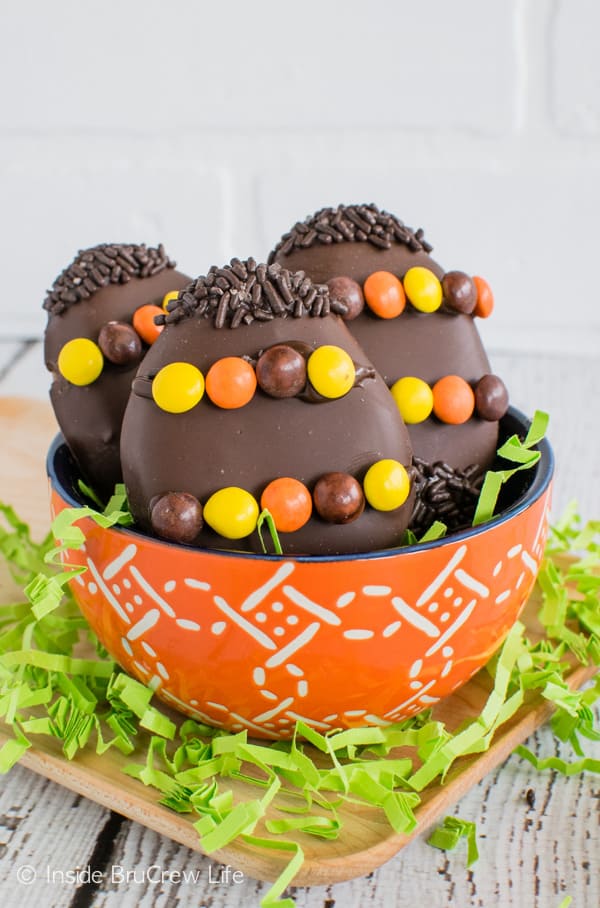 An orange bowl surrounded by green Easter grass and filled with three homemade Reese's Eggs decorated with candy and sprinkles.