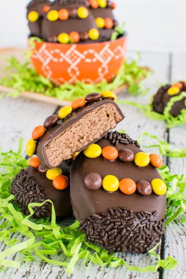 Three homemade Reese's eggs stacked on top of each other on a white board with green Easter grass. The top egg is cut in half showing the inside filling.