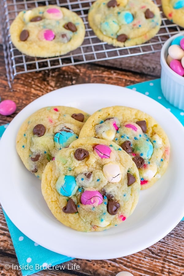 Overhead picture of a white plate with three vanilla pudding cookies loaded with candy and sprinkles on it