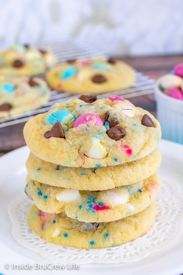 A stack of four chocolate chip pudding cookies with M&M's and sprinkles stacked on top of each other on a white plate