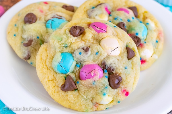 A white plate with three chocolate chip pudding cookies with M&M's and sprinkles on it