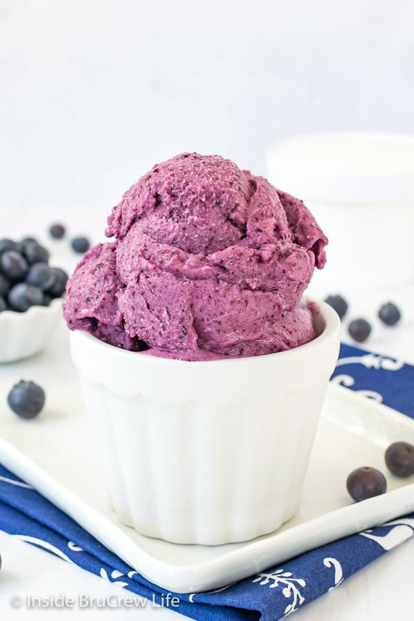A white bowl on a white plate filled with scoops of blueberry banana frozen yogurt