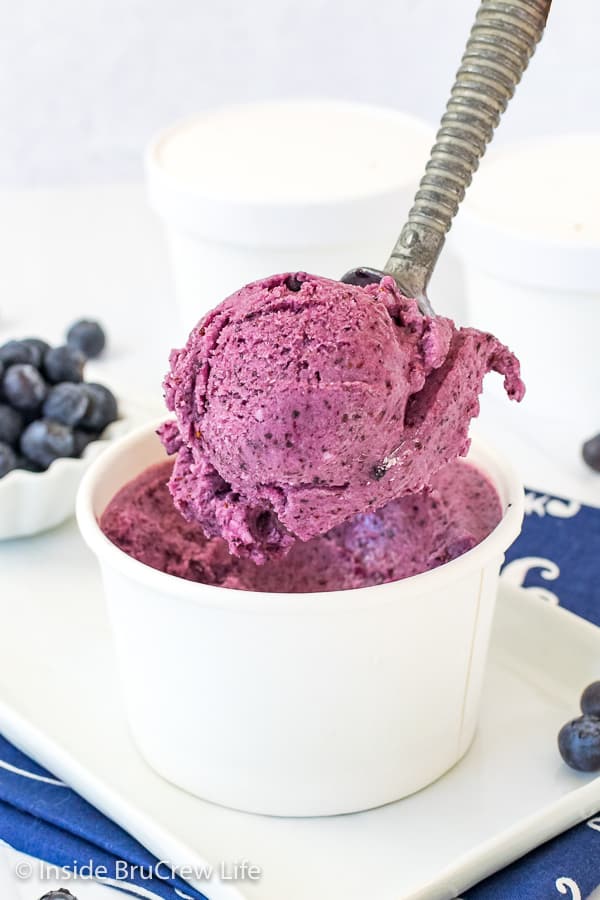 A white bowl filled with blueberry banana frozen yogurt with a spoon lifting out a scoop