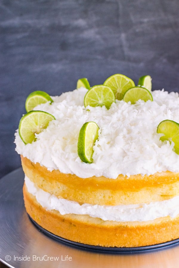 A close up picture of the side of a key lime cake with coconut frosting in the middle and on top and decorated with key lime slices