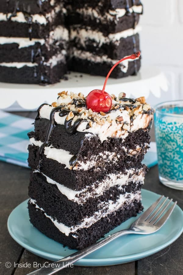 Dark Chocolate Layer Cake - 4 layers of cake and frosting topped with hot fudge, pecans, and cherries is perfect for any celebration! This is an awesome dessert recipe.