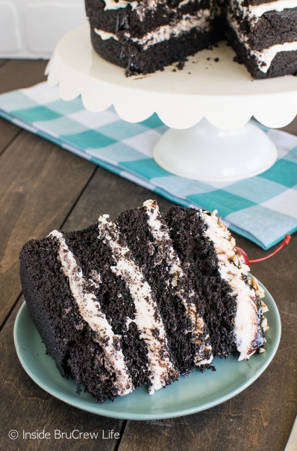 Layers of cake and frosting topped with hot fudge, pecans, and cherries make this Dark Chocolate Layer Cake the perfect dessert recipe!