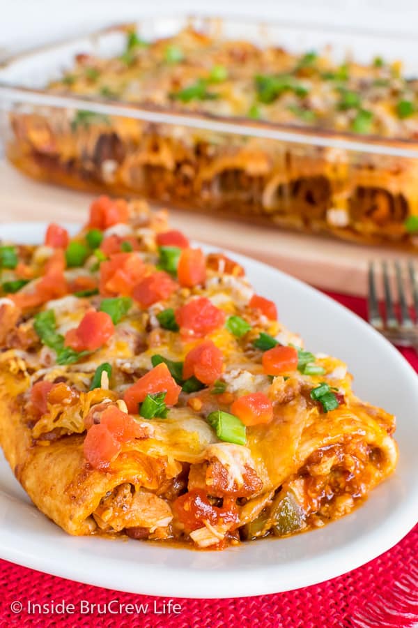 A white plate on a red towel with two Monterey Chicken Enchiladas on it topped with green onions and tomatoes