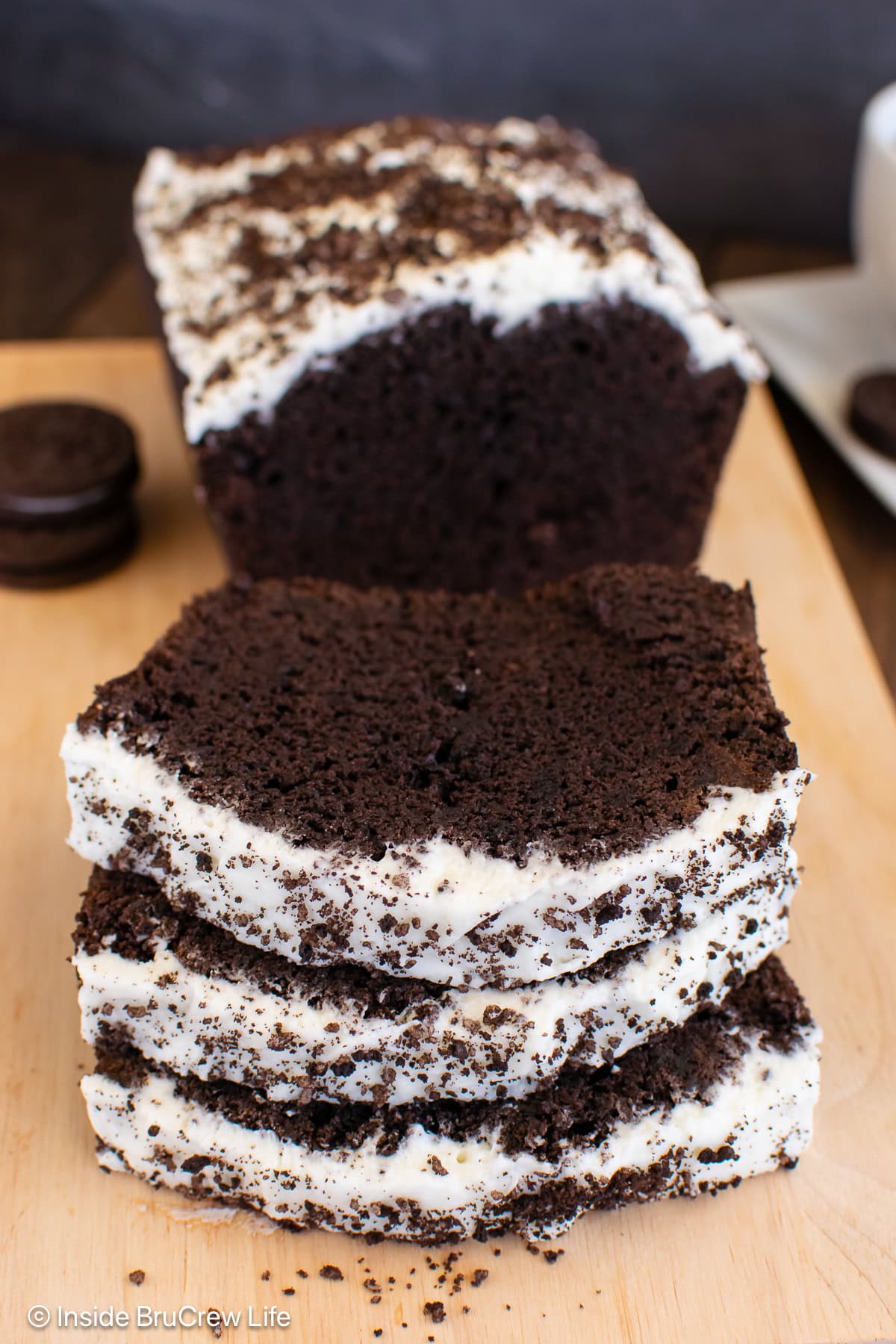 A sliced loaf of Oreo banana bread with frosting on a cutting board.