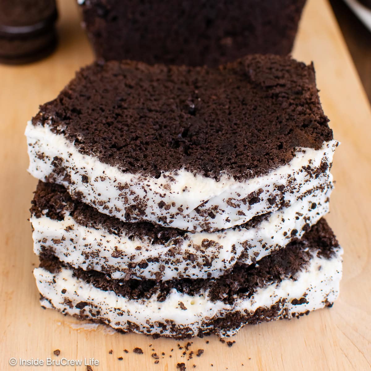 A sliced loaf of Oreo banana bread with frosting on a cutting board.