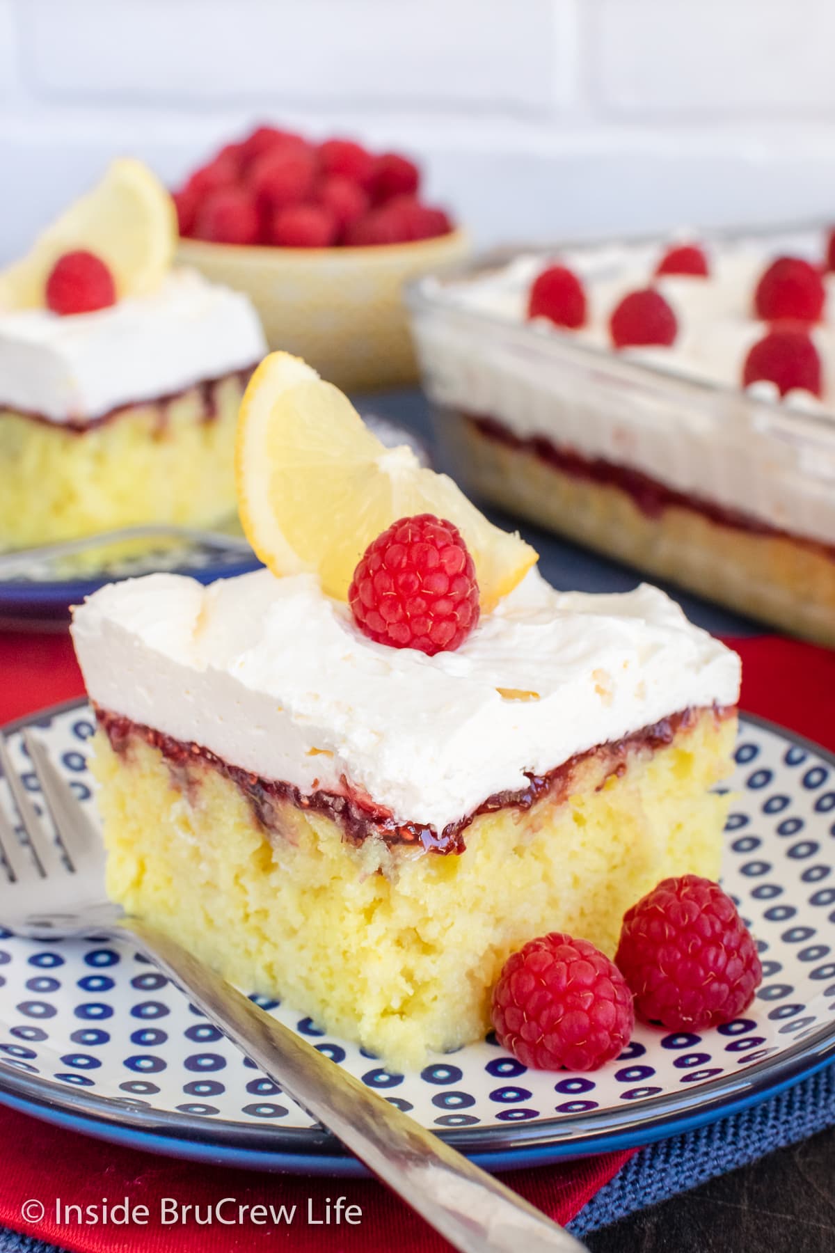 Lemon cake squares with raspberry and lemon topping on two plates.