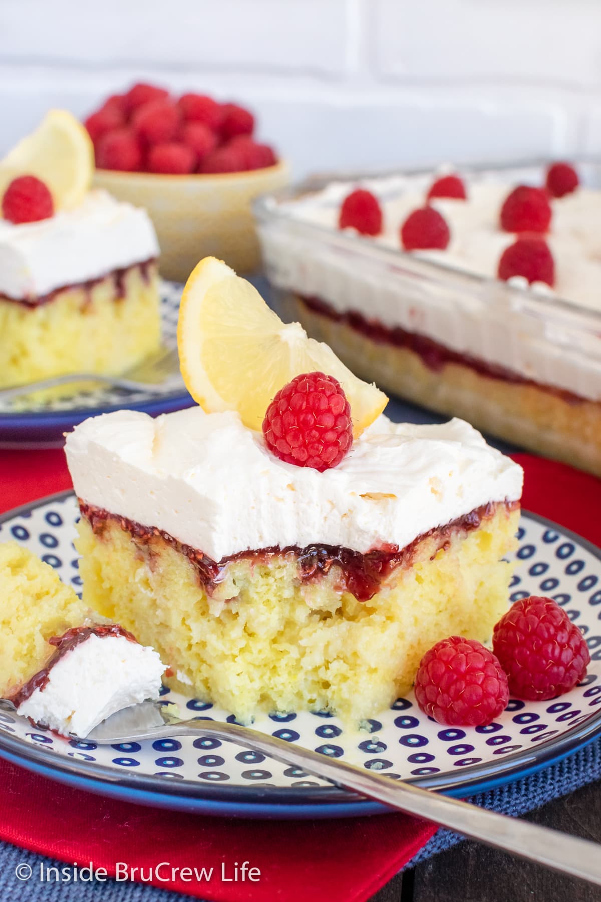 Lemon cake squares with raspberry and lemon topping on two plates.