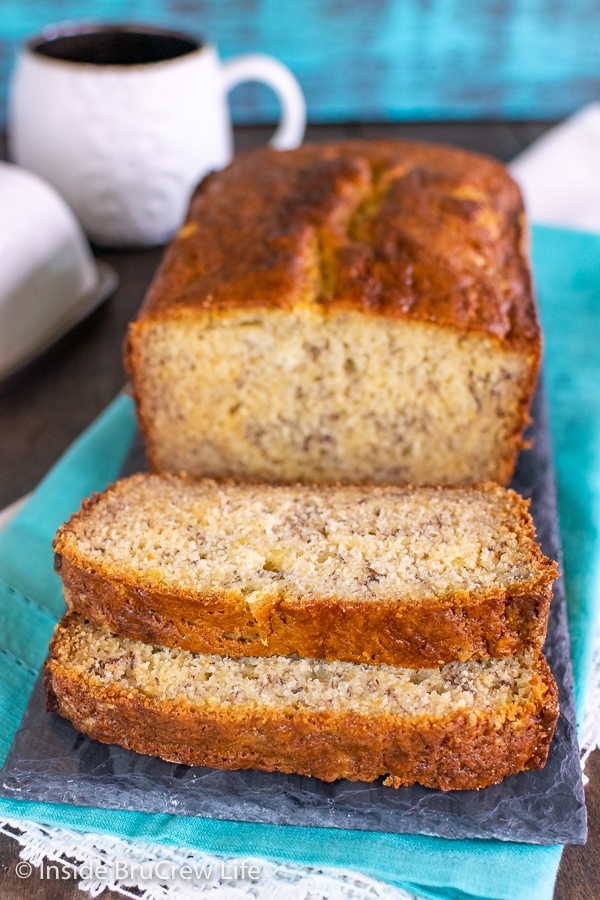 A loaf of sour cream banana bread with two slices down in front on a slate board