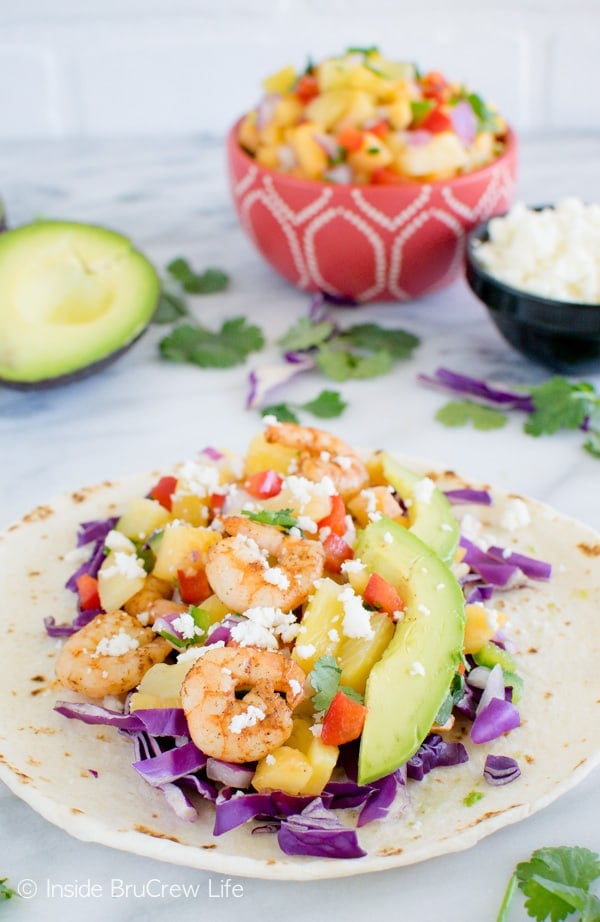 Close up picture of an open face tortilla loaded with shrimp, fruit salsa, cabbage, and cheese