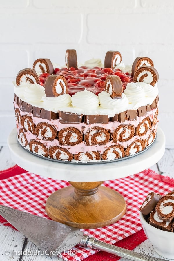 A white cake plate with a full No Bake Cherry Swiss Rolls Cake on it topped with cherry pie filling