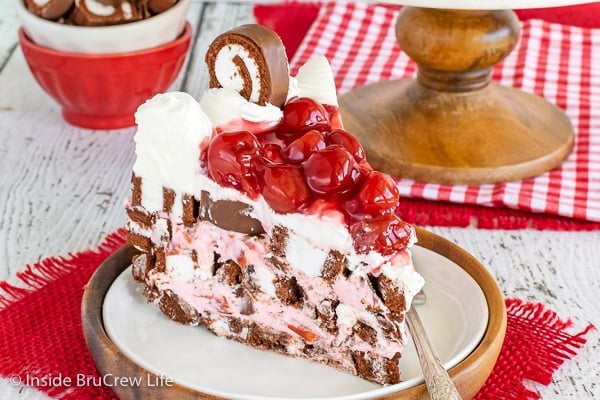 A white plate with a slice of cherry swiss rolls cake topped with cherries on it