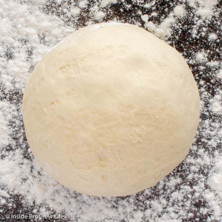 A floured counter with a ball of dough on it.