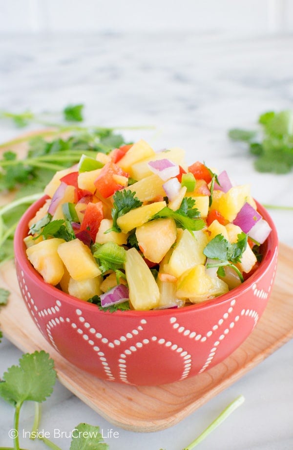 A red bowl on a wood platter filled with pineapple peach salsa.