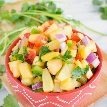 A red bowl full of pineapple peach salsa with some cilantro in the background.