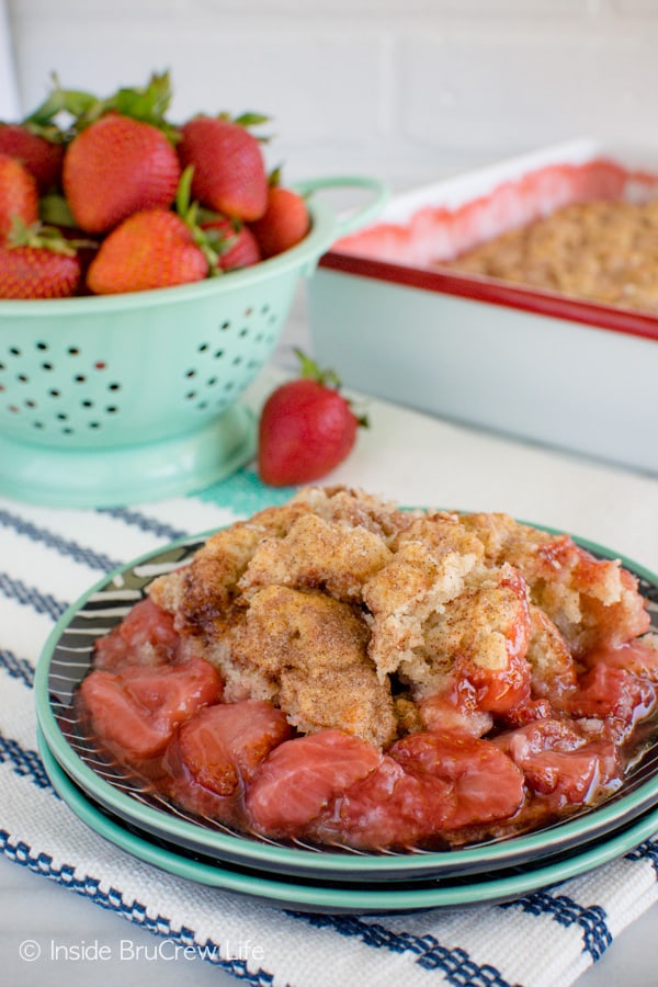 A plate filled with strawberry cobbler and the pan of cobbler and more berries behind it
