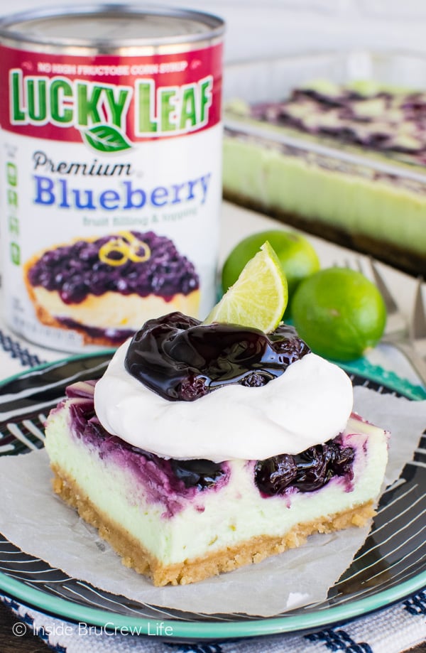 A square of Key Lime Blueberry Cheesecake Bars topped with Cool Whip and more blueberry pie filling on a black plate