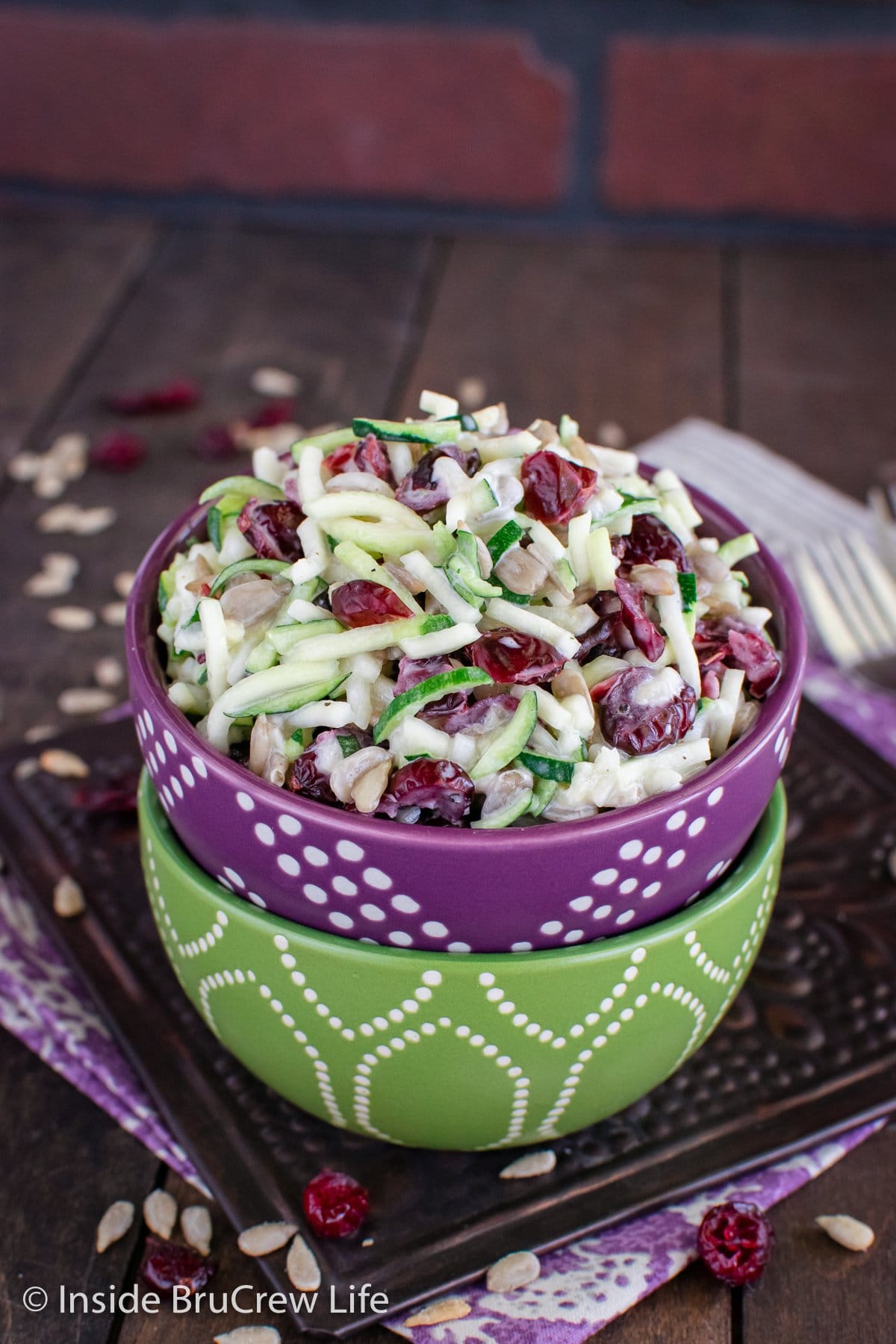 A stack of green and purple bowls filled with zucchini noodles and cranberries.