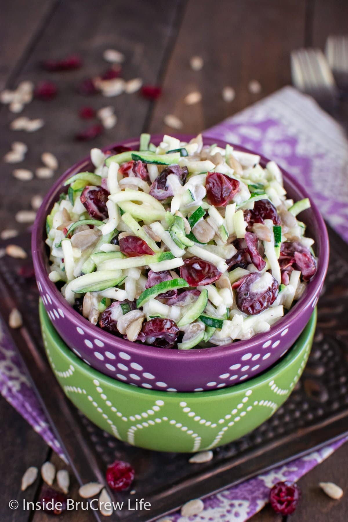 A stack of green and purple bowls filled with zucchini noodles and cranberries.