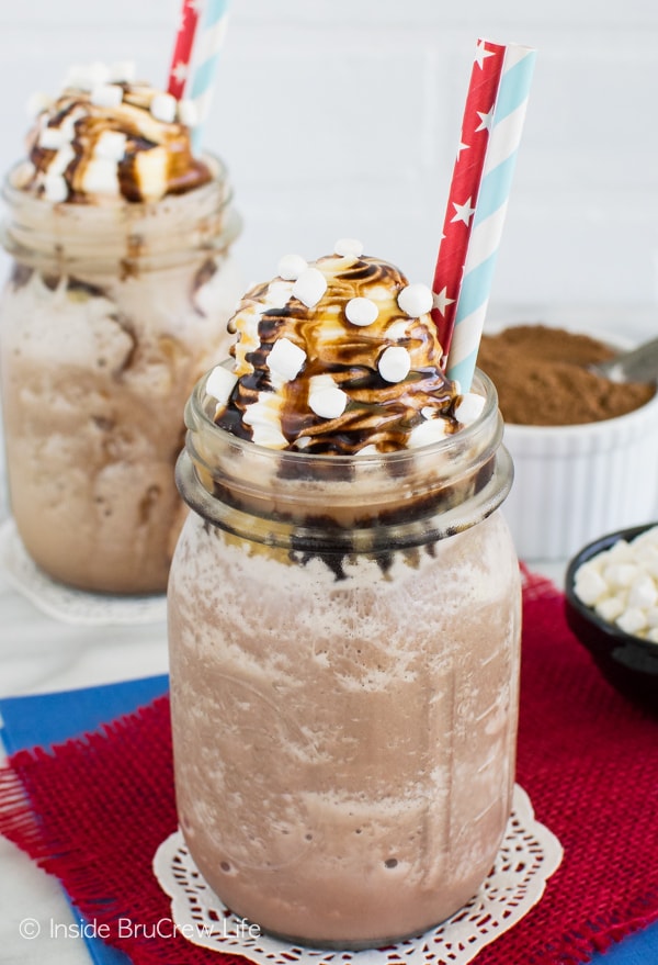 Two glasses of Frozen Hot Chocolate with red straws and chocolate and caramel drizzles on top.