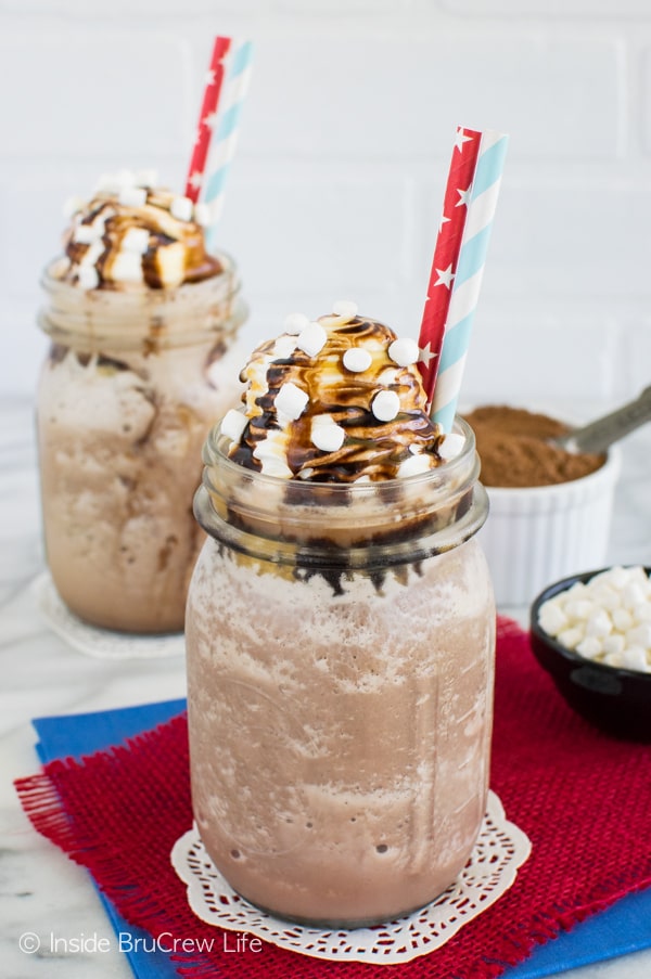 Two glasses filled with Frozen Hot Chocolate drizzled with caramel and chocolate with two straws in each.