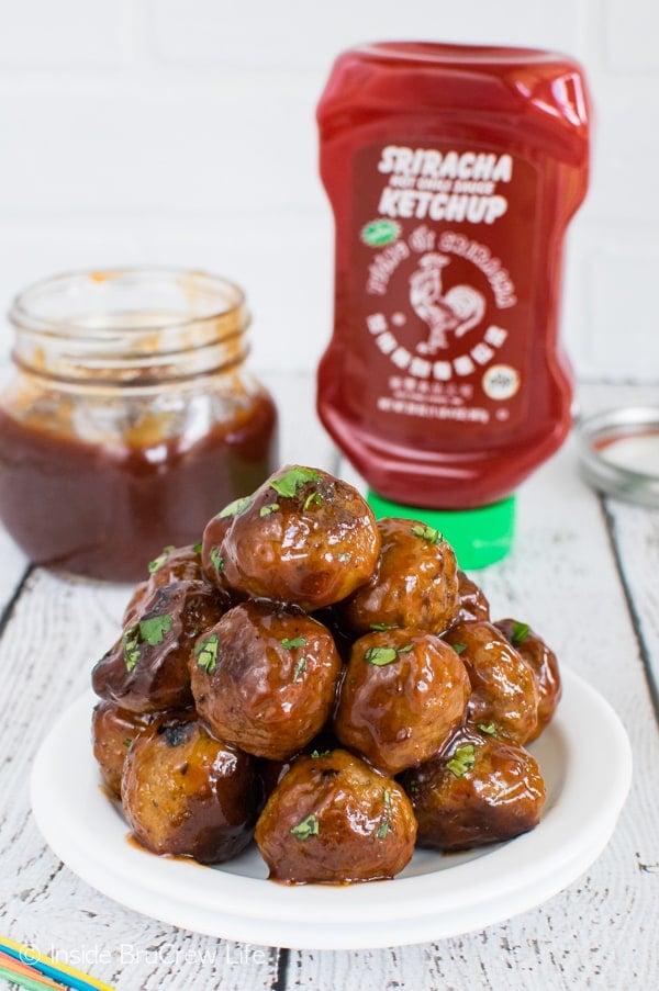 A white plate with a stack of honey sriracha barbecue meatballs on it and a jar of sauce behind it