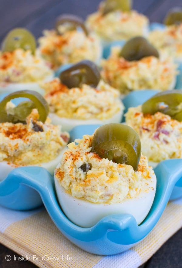 A glass blue egg container with bacon, jalapeño deviled eggs in it.
