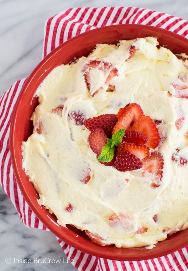 A red bowl filled with lemon fluff cheesecake salad and strawberries.