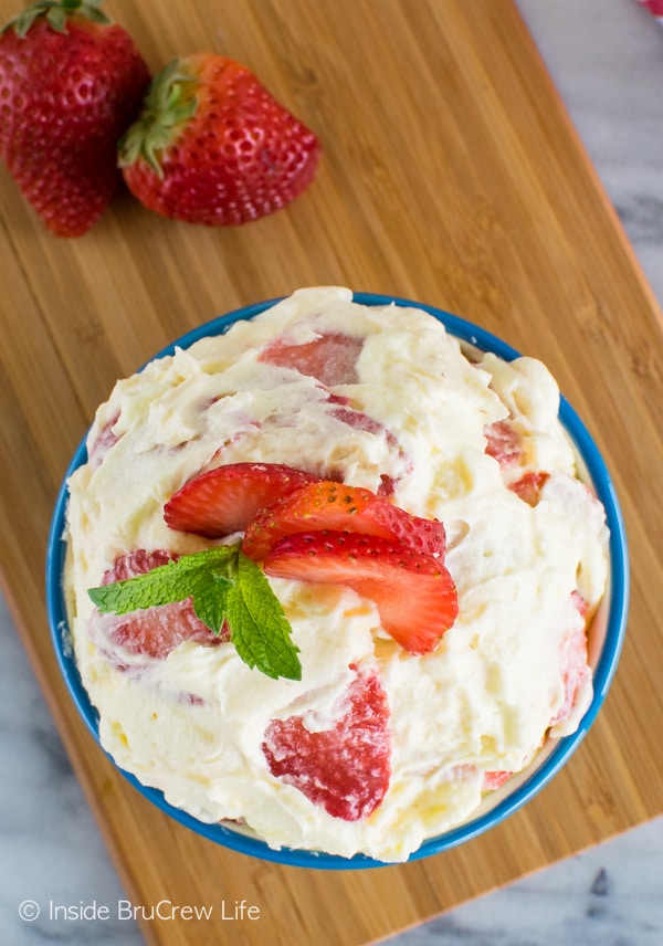 Overhead picture of a blue bowl on a wooden board filled with creamy lemon fluff and strawberry slices.