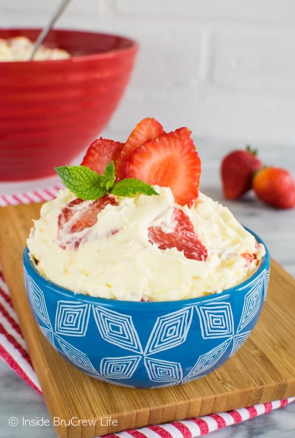 A blue bowl filled with lemon fluff cheesecake salad topped with strawberry slices.