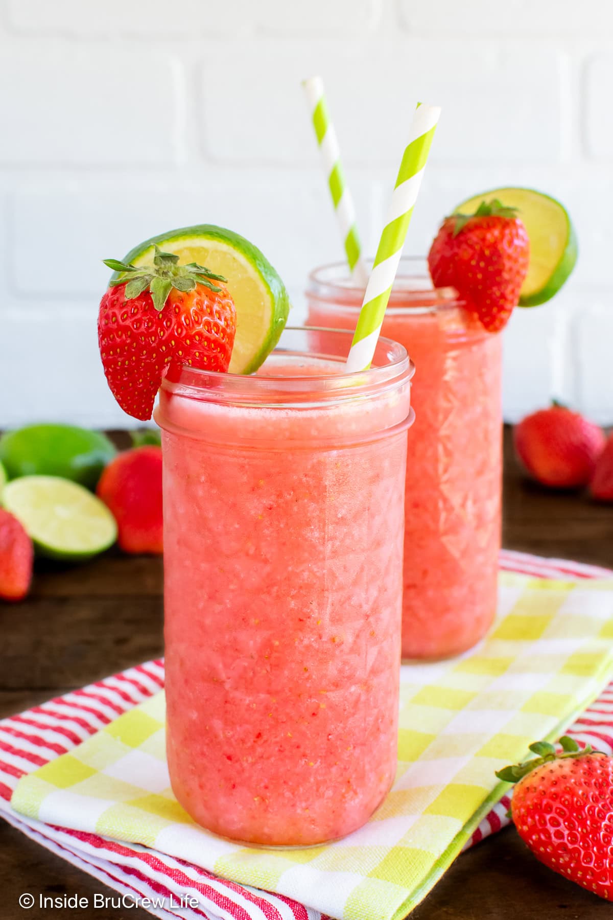 Two strawberry slushies with straws and lime slices.