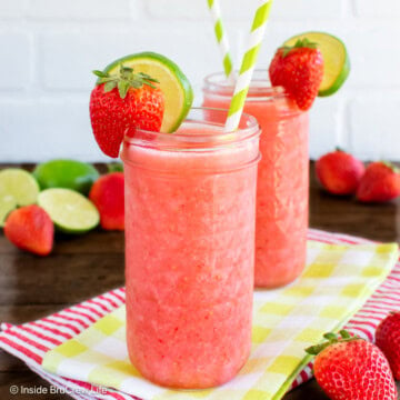 Two strawberry slushies with straws and lime slices.