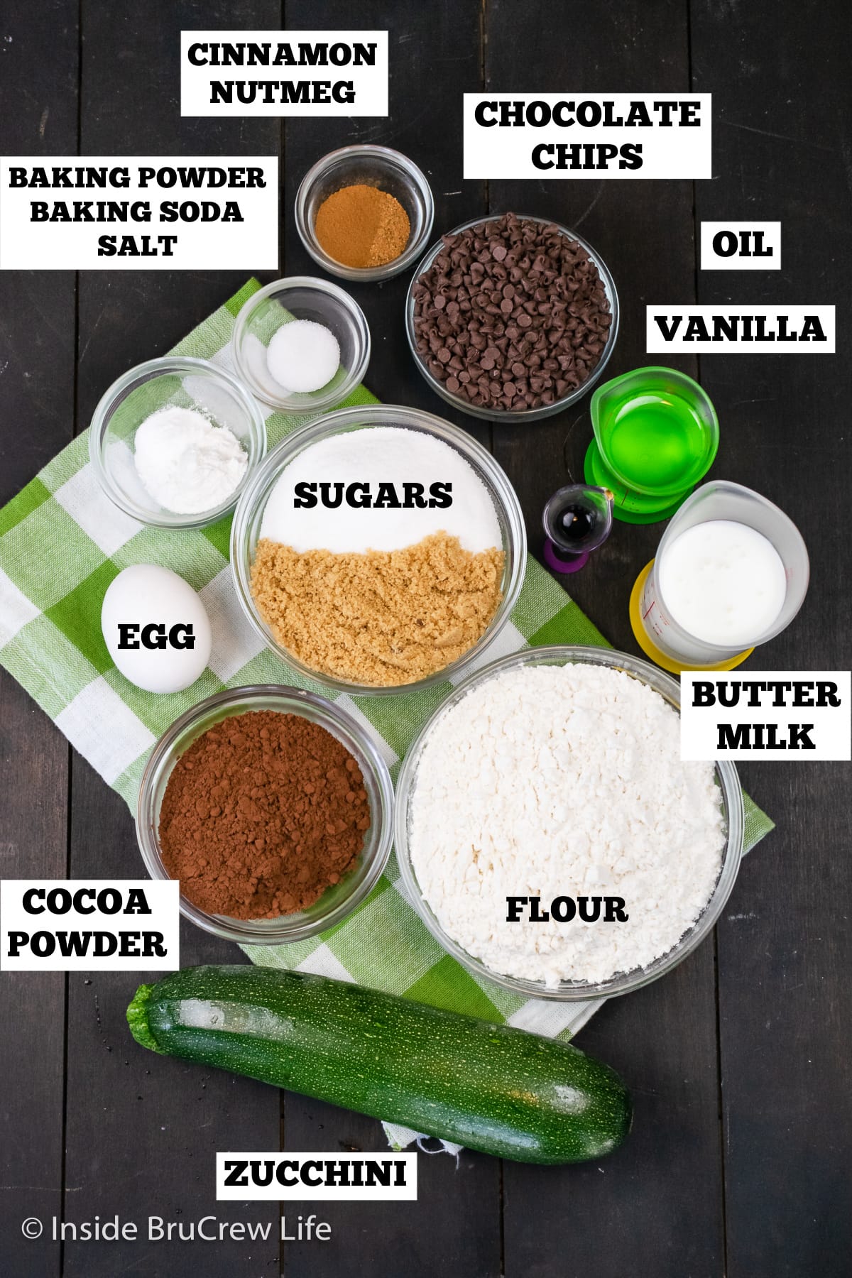 A brown board with bowls of ingredients needed to make a zucchini bread with chocolate.