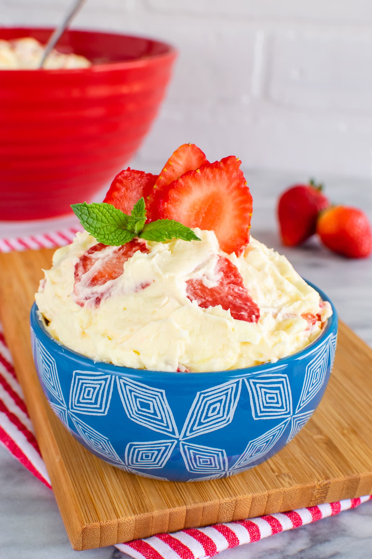 A blue bowl filled with lemon fluff dessert and fresh strawberries.