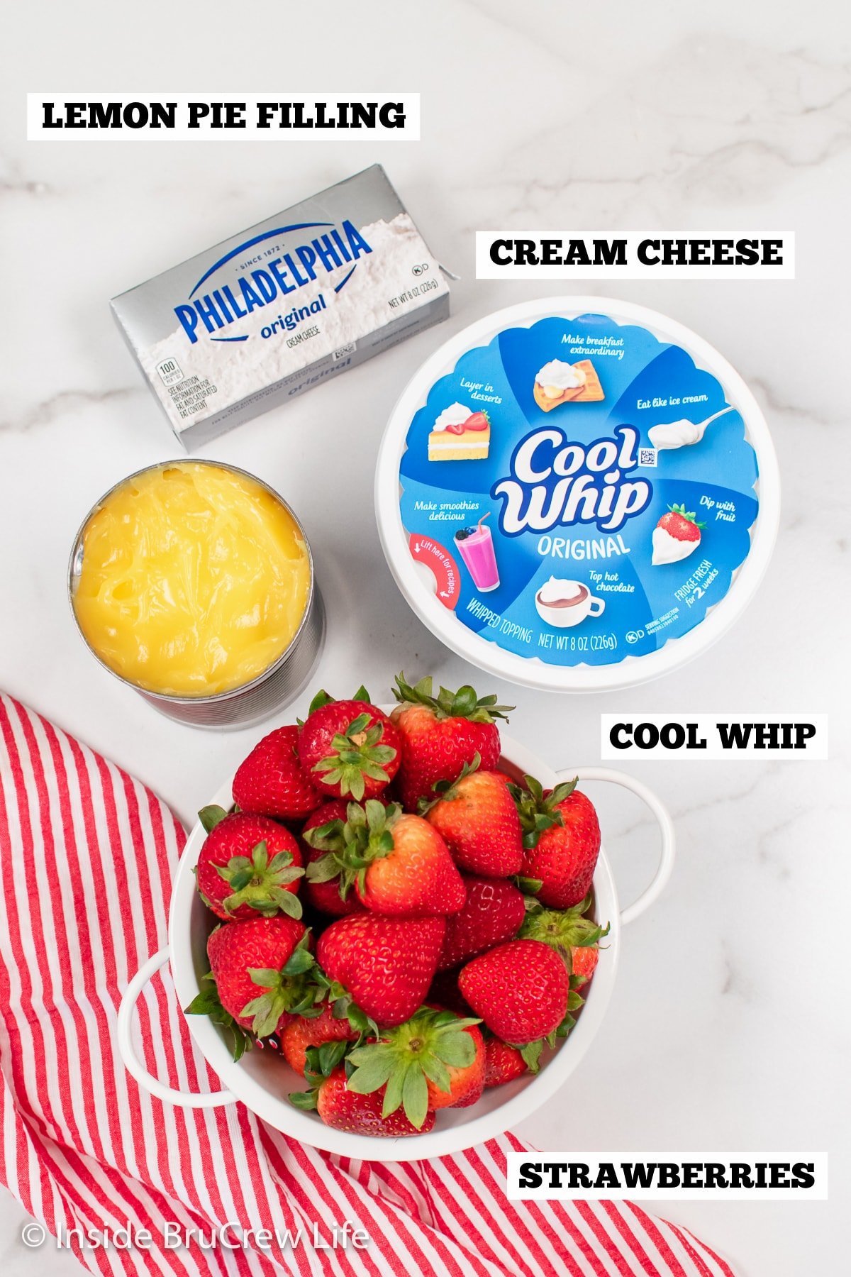 A white board with ingredients needed to make a fluff salad with lemon pie filling and strawberries.