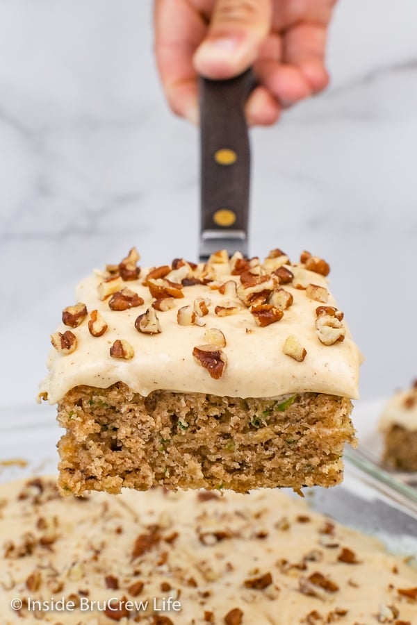 A spatula lifting a square of frosted zucchini cake out of a cake pan.