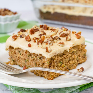 A white plate with a slice of zucchini banana cake topped with caramel frosting and pecans.