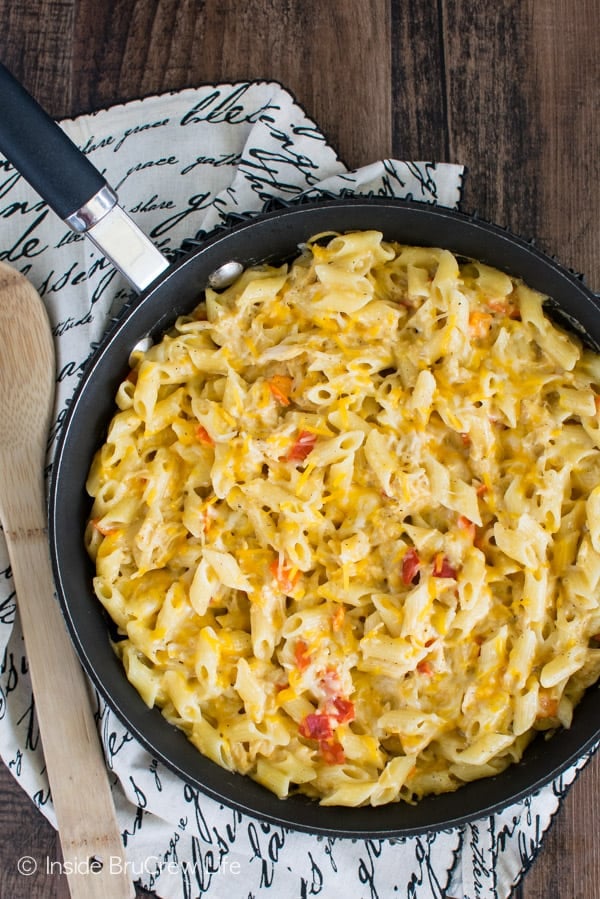 Overhead picture of a skillet with cheesy chicken pasta in it and a white towel under it.