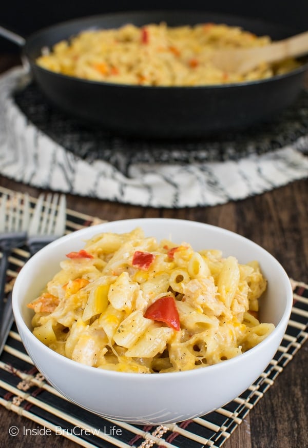 A white bowl filled with chicken pasta and the rest of the pasta behind it in a black skillet.