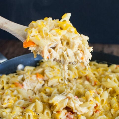 A skillet filled with cheesy chicken pasta and a spoon lifting out a big cheesy spoonful.
